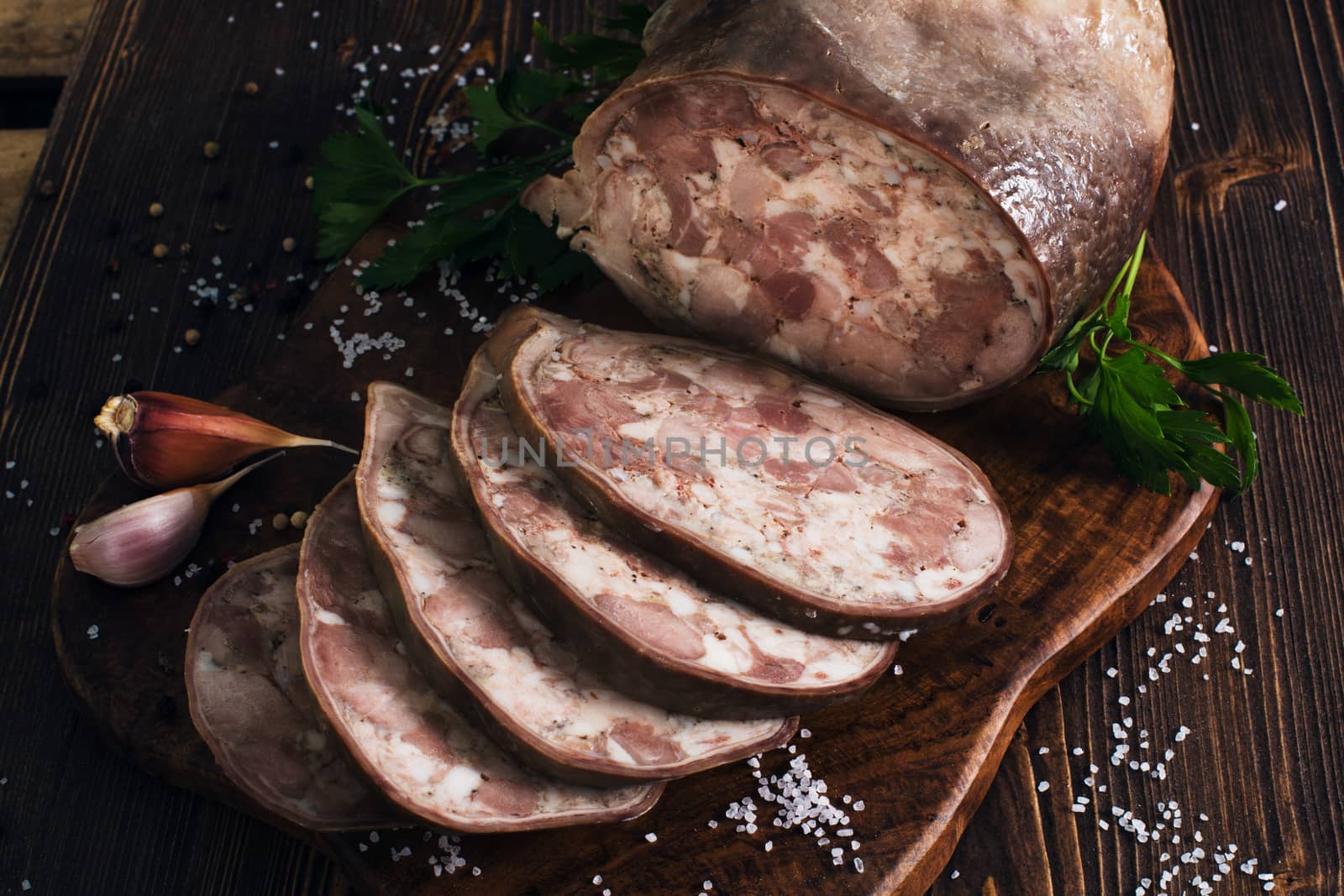 Sliced pork saltisons with herbs on a slate cutting board on wooden background