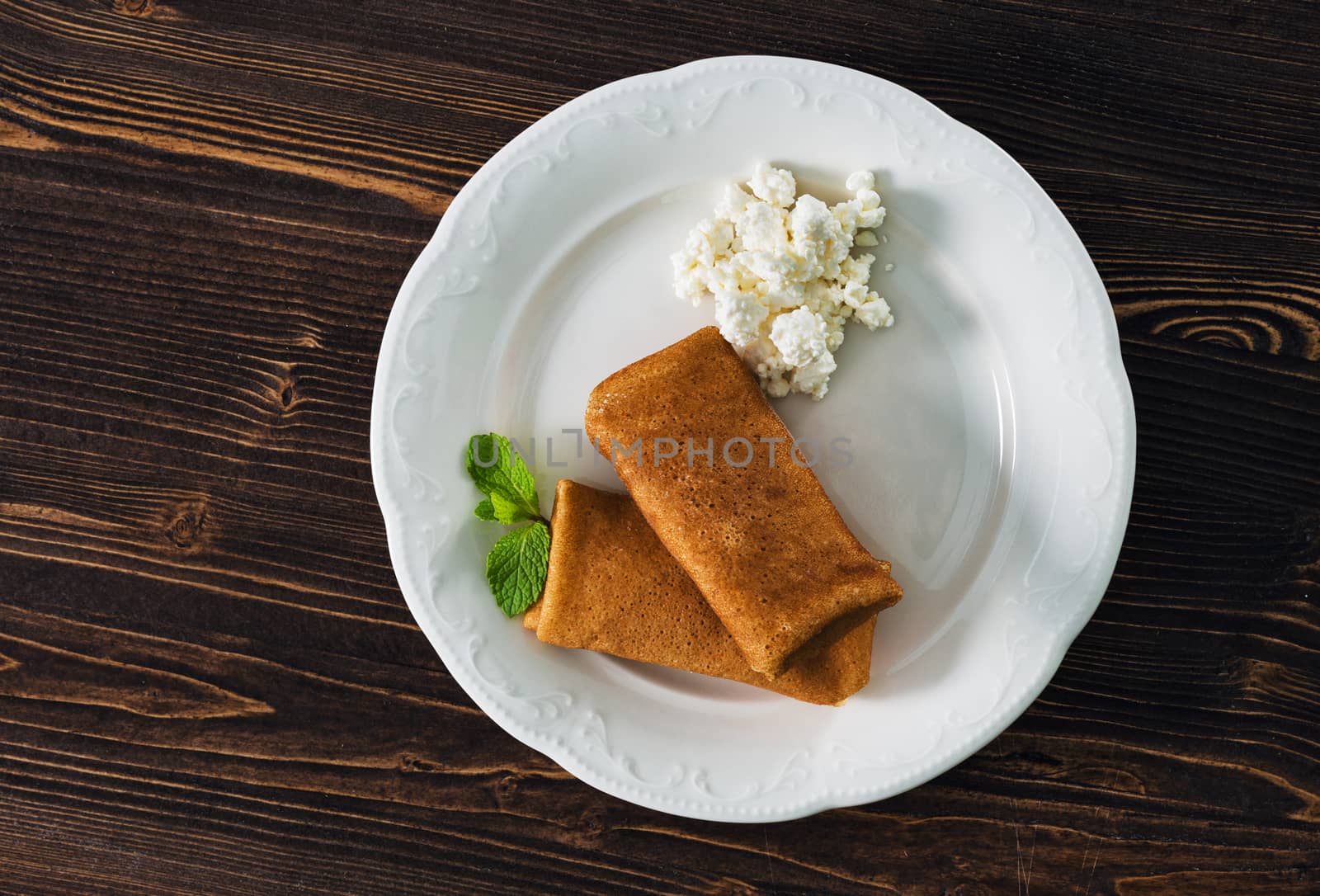 Pancakes with condensed milk on a plate, wooden background