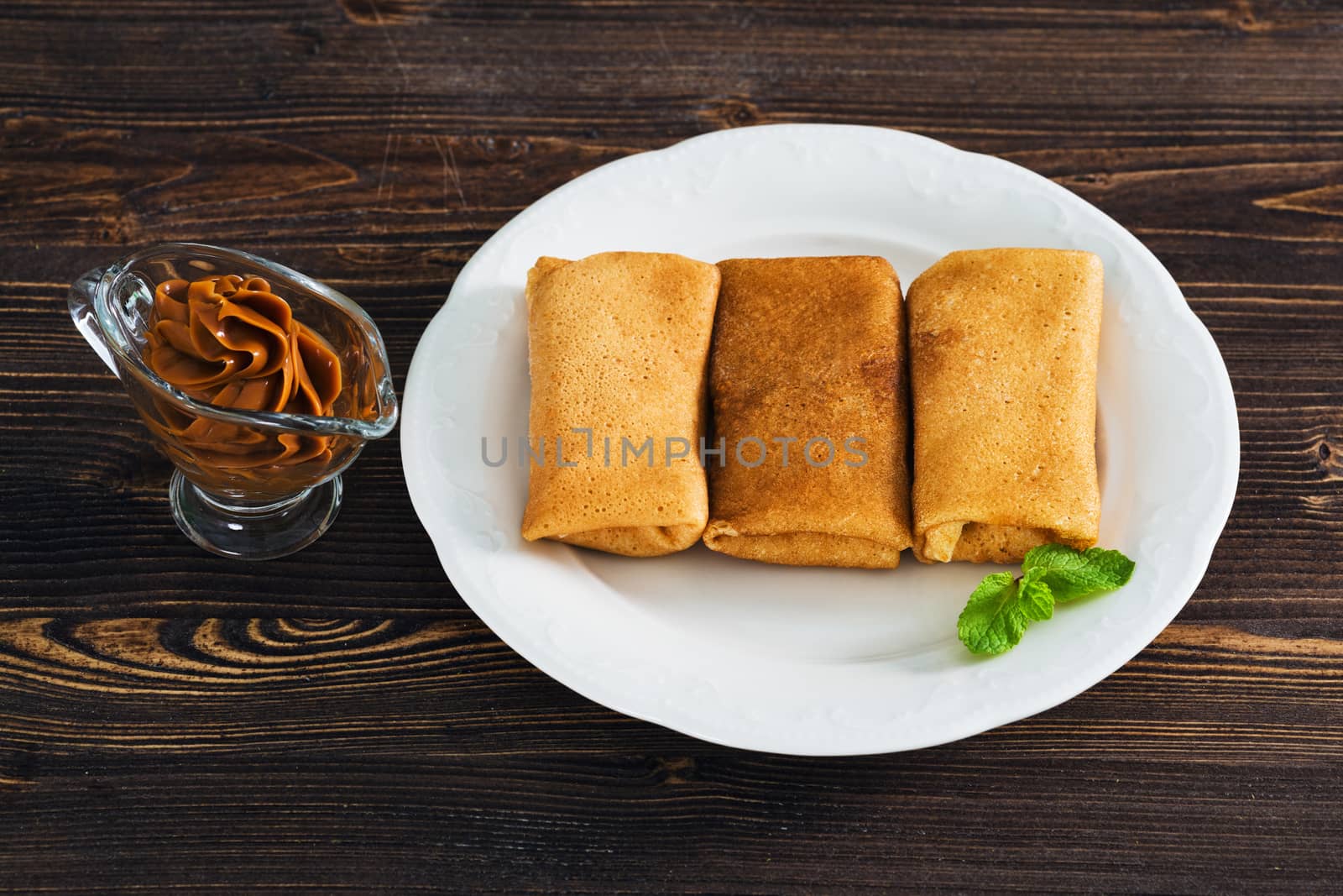 Pancakes with condensed milk on a plate, wooden background