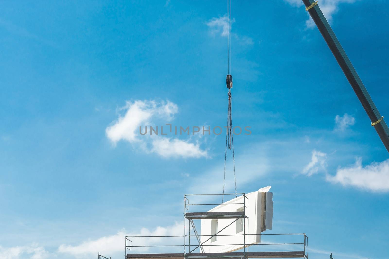 A wall part of a prefabricated house on a crane against blue sky.