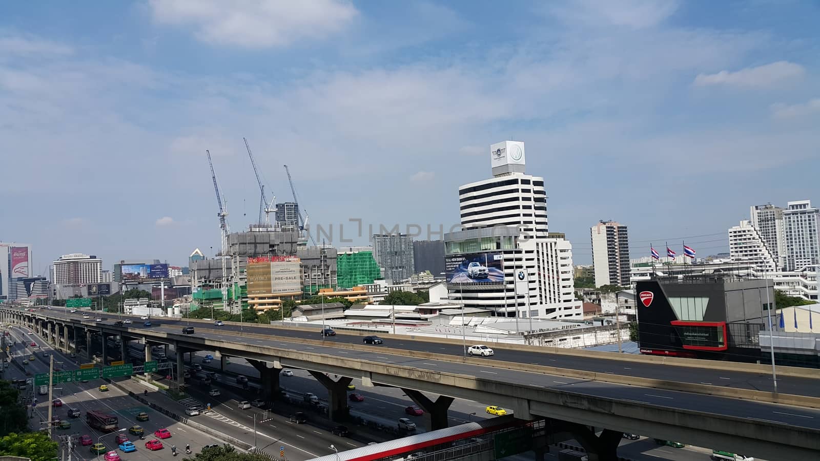 Bangkok, Thailand - November 04, 2016: People are moving on their vehicle on both express way and normal way. The photo also shown the under-construction building with working crane, the car showroom and the motorcycle showroom