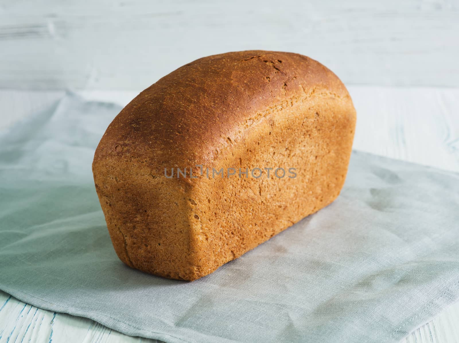 Loaf of rye bread on towel on wooden background