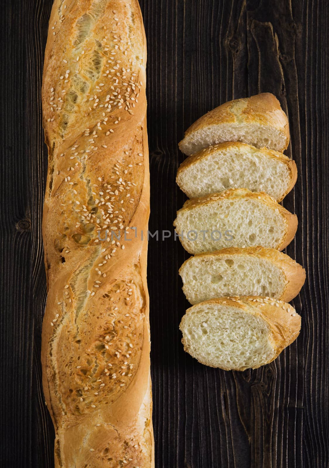 Top view of a sliced of baguette, dark wooden background