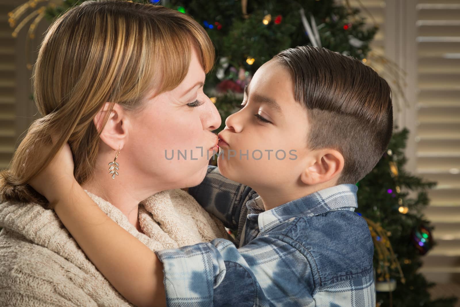 Happy Mother and Mixed Race Son Hug Near Their Christmas Tree.