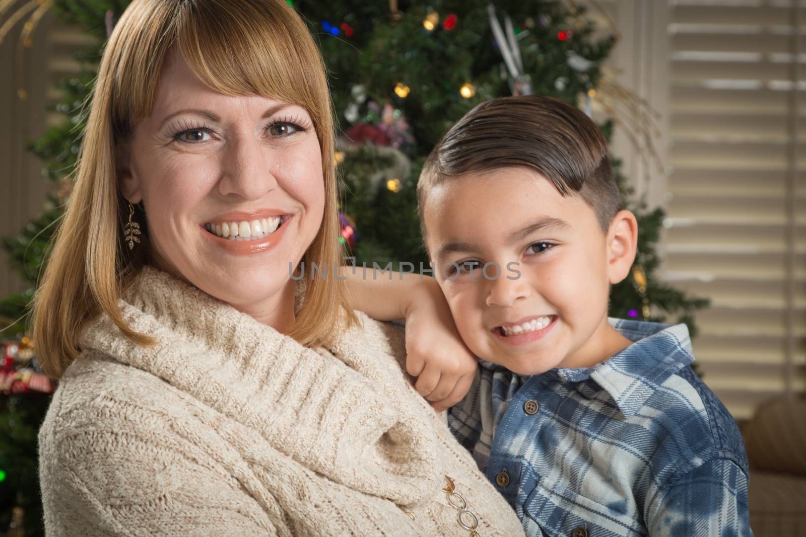 Happy Mother and Mixed Race Son Hug Near Their Christmas Tree.