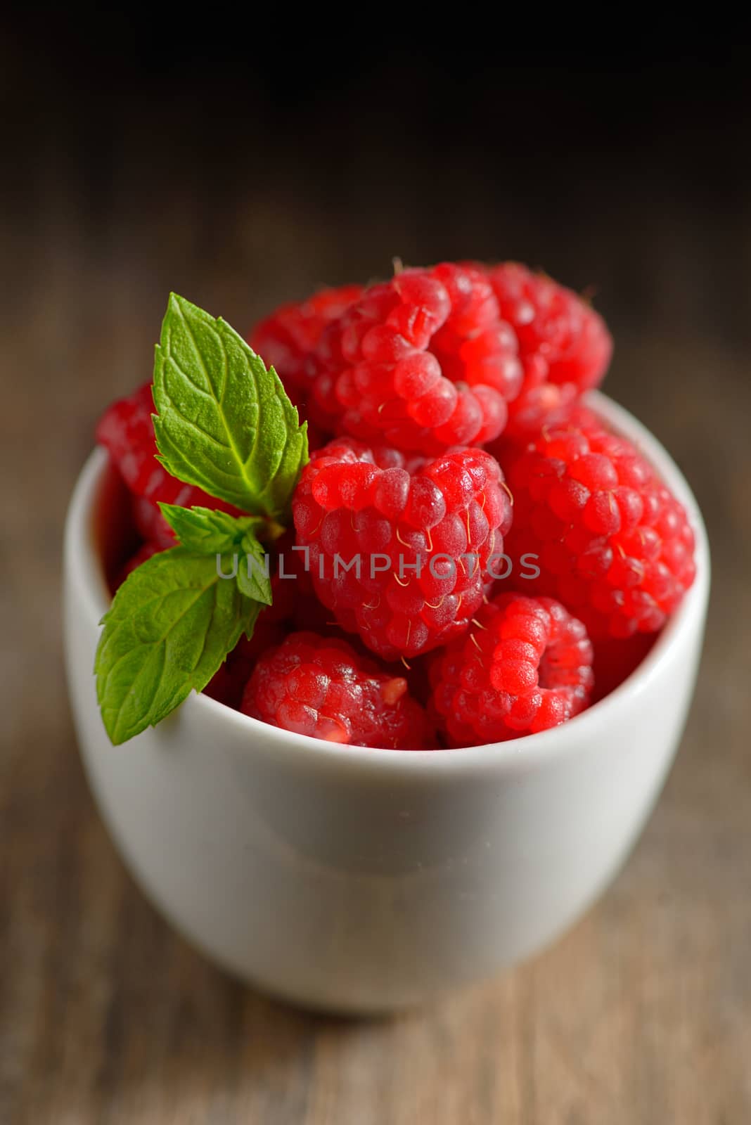 ripe and fresh raspberry in white cup on wooden table