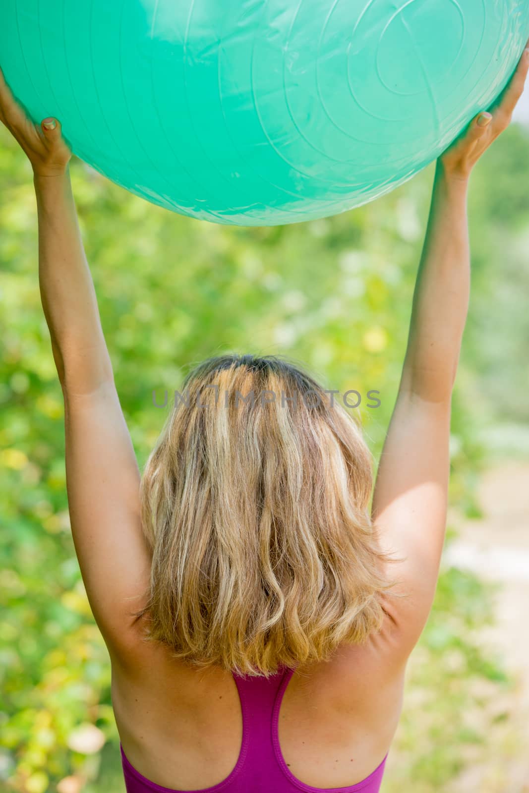 A blonde woman carring the exercise ball while performing the mountain yoga pose