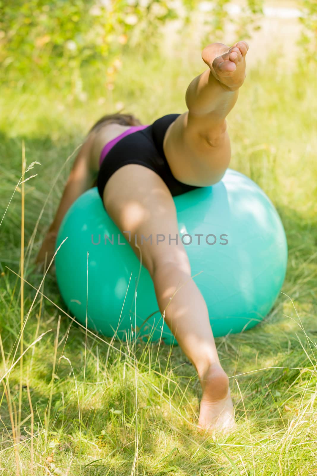 a woman performing the leg-high yoga pose on an exercise ball outside.