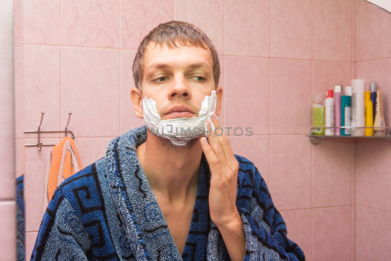 The young man gets shaving foam on his cheeks