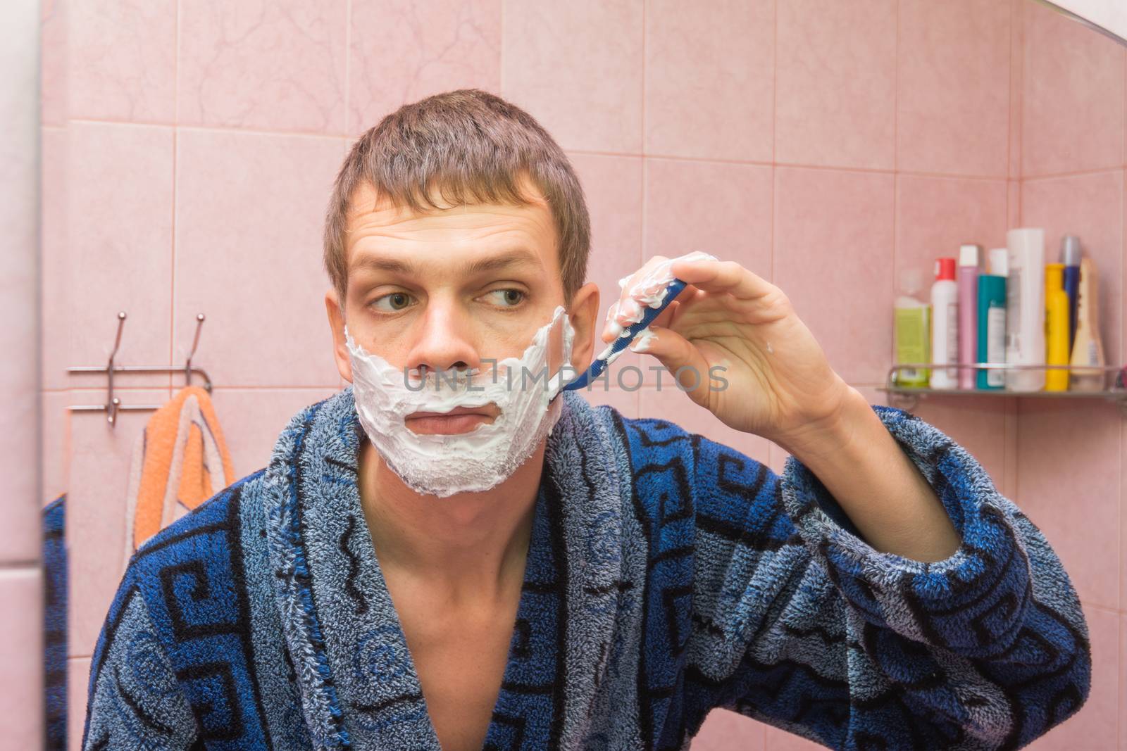 Young man shaves the stubble on his cheek