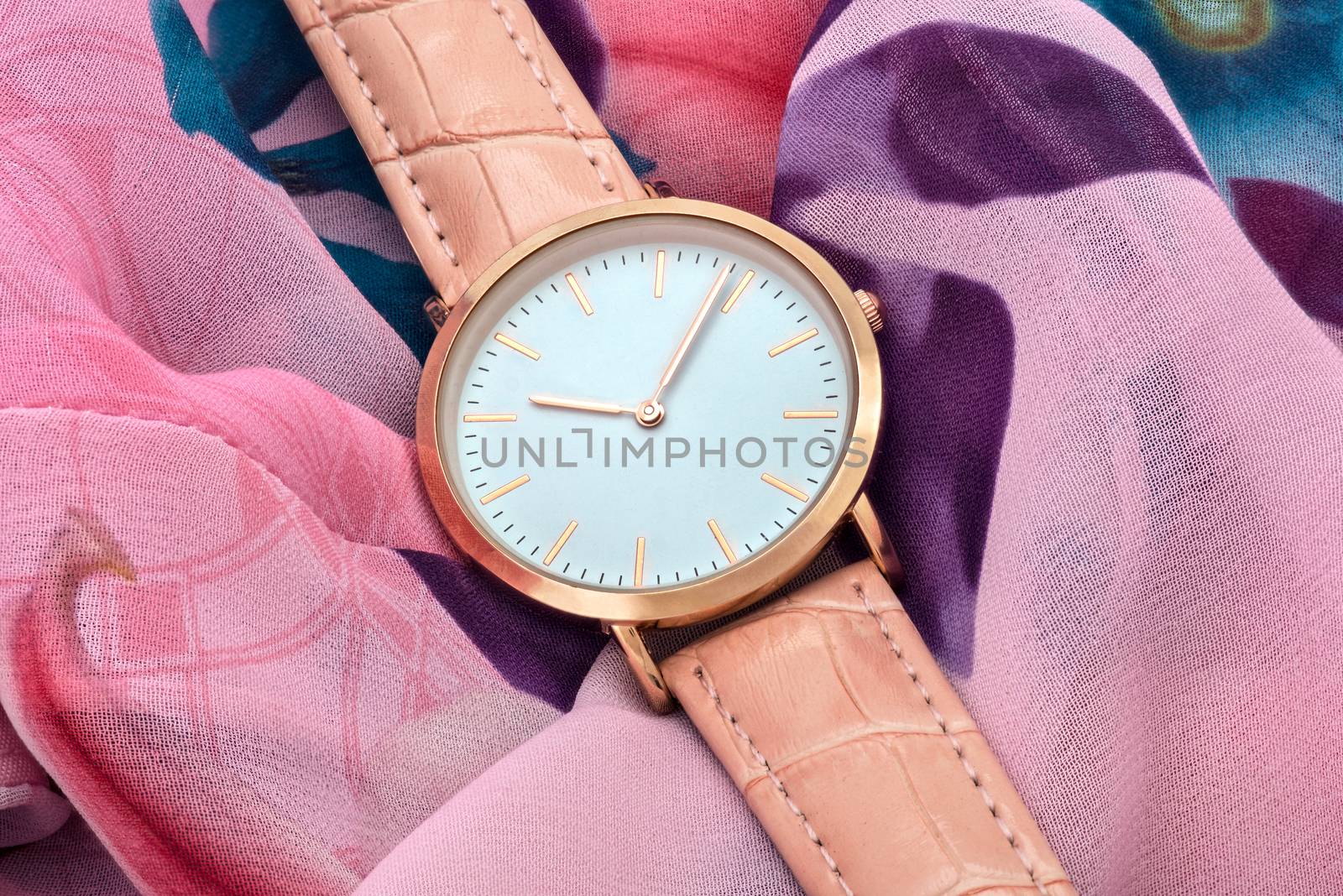 Classic pink wrist watch on colourful silk fabric background