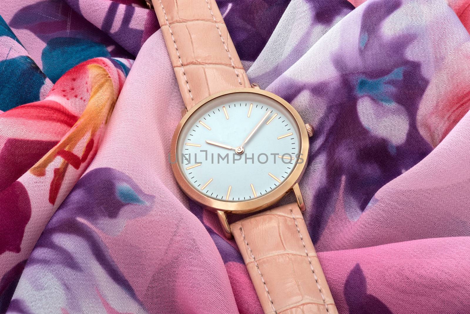 Classic pink wrist watch on colourful silk fabric background