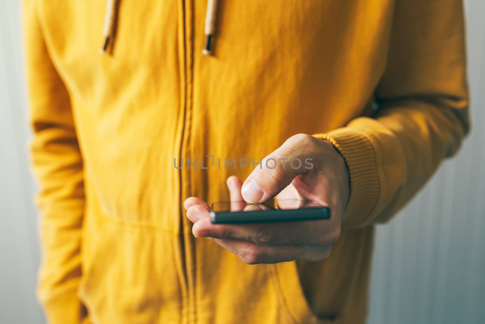 Young man in yellow shirt using smartphone by stevanovicigor