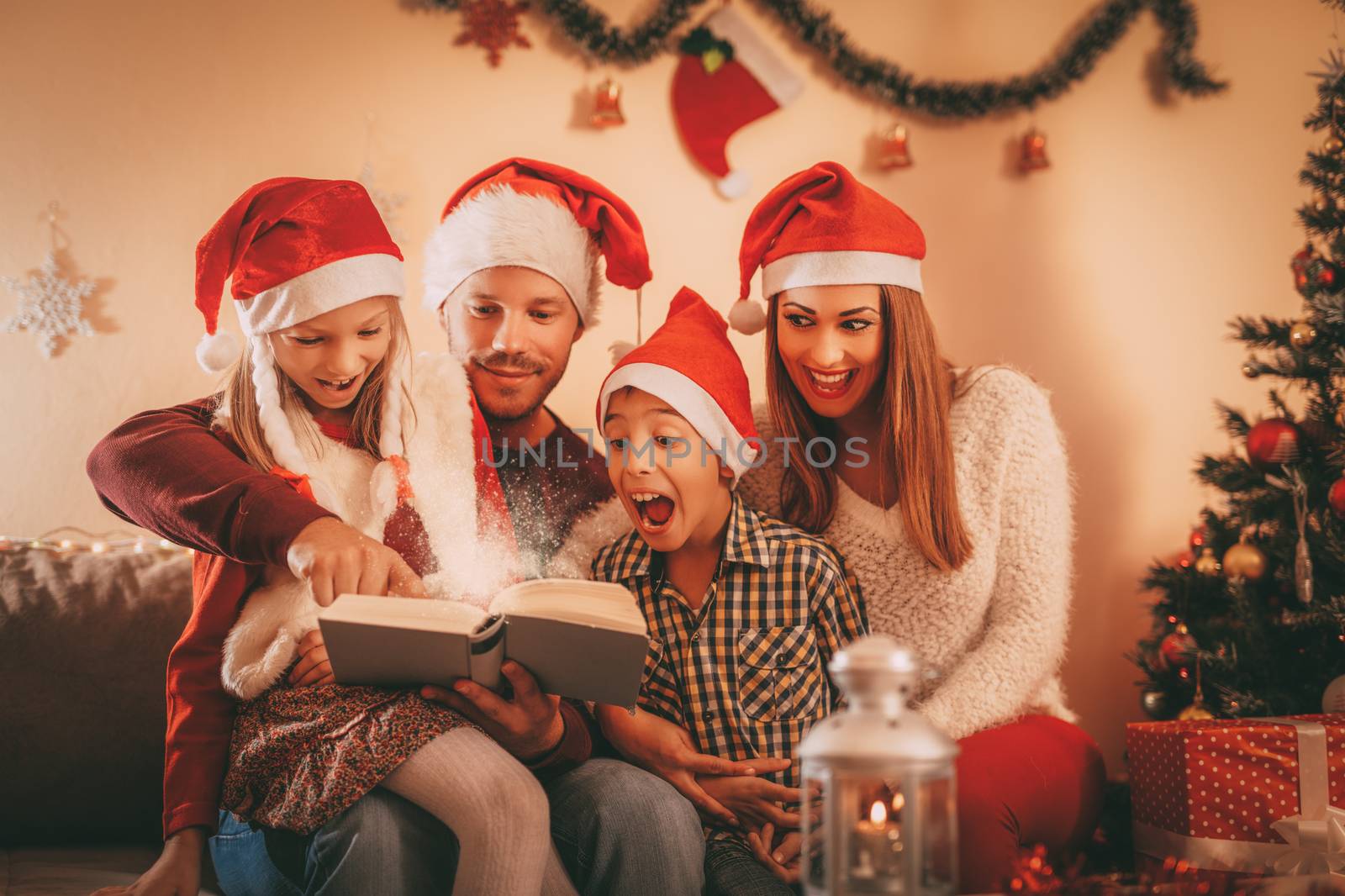 Beautiful smiling family of four with santa hat reading book at the home.