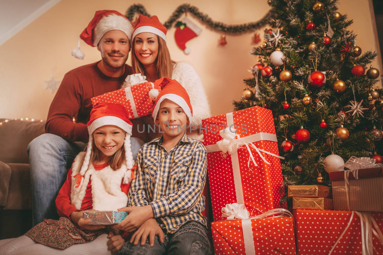 Beautiful happy family wearing santa hat and exchanging Christmas gifts at home. Looking at camera.