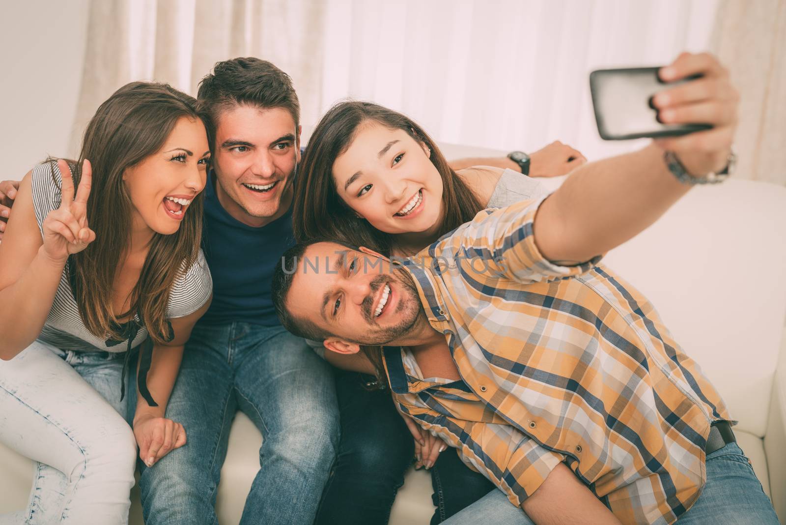 Four cheerful best friends having nice time in an apartment and taking selfie.