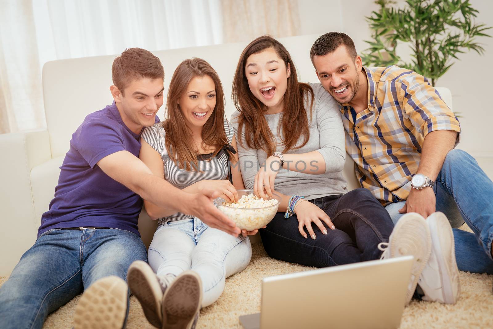 Four cheerful best friends having nice time in an apartment. They are watching movie together.