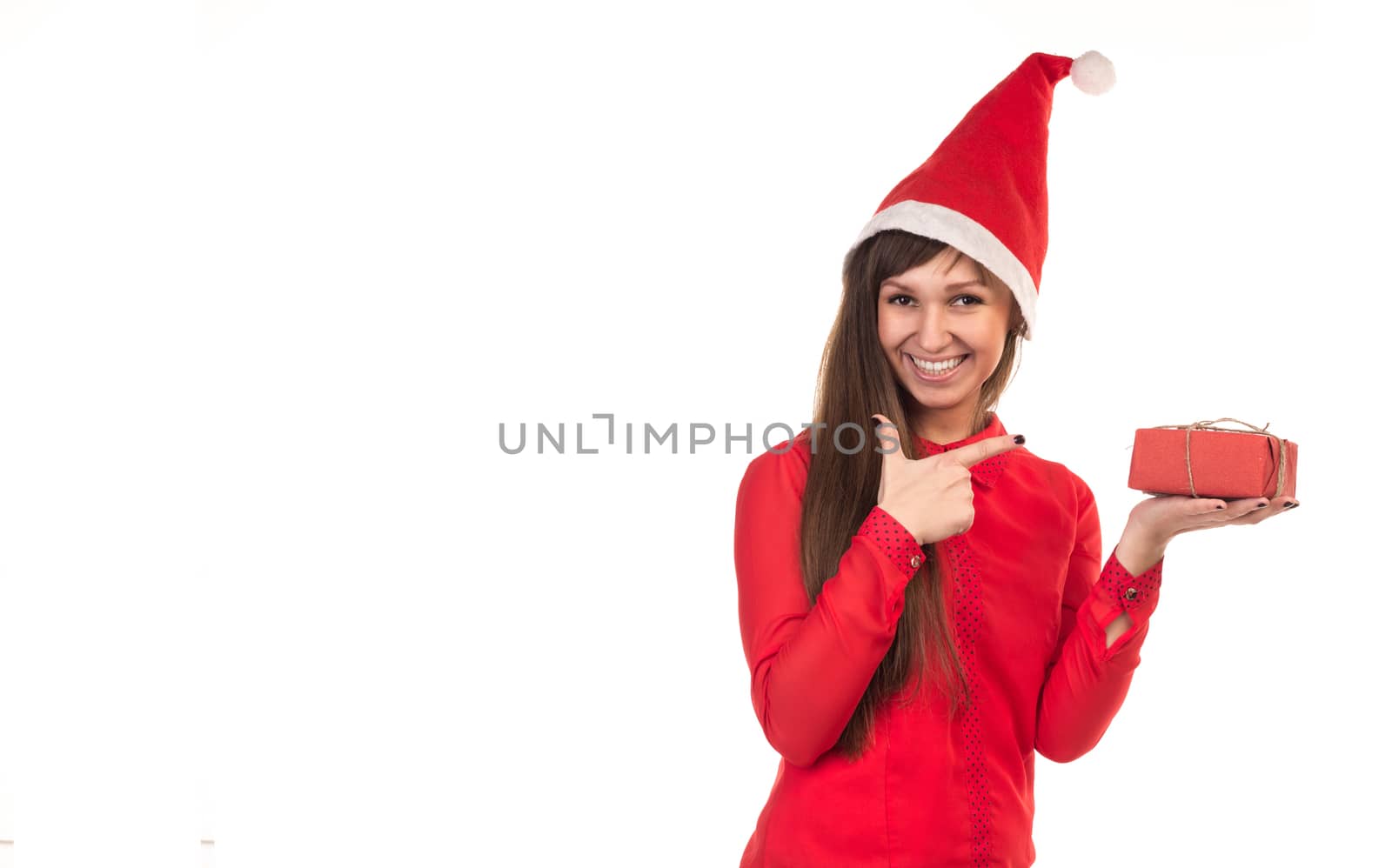 Young long-haired woman in red christmas cap points with her finger to red gift box