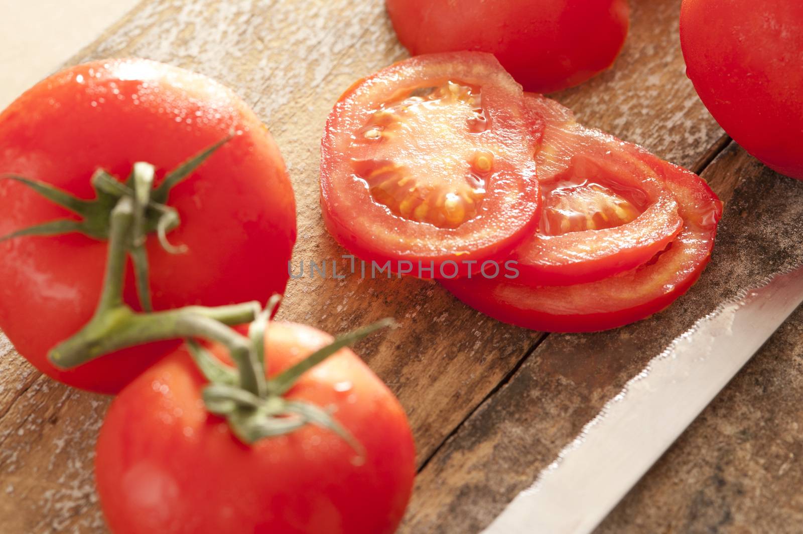 Freshly washed ripe red tomatoes with water droplets whole on the vine and sliced on a wooden cutting board with a kitchen knife
