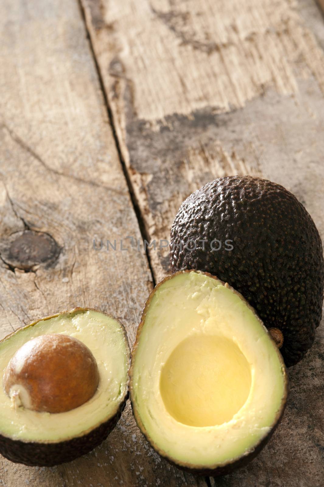 Ripe halved and whole avocado pear on a rustic wooden table ready to be served as a salad ingredient, high angle view with copy space