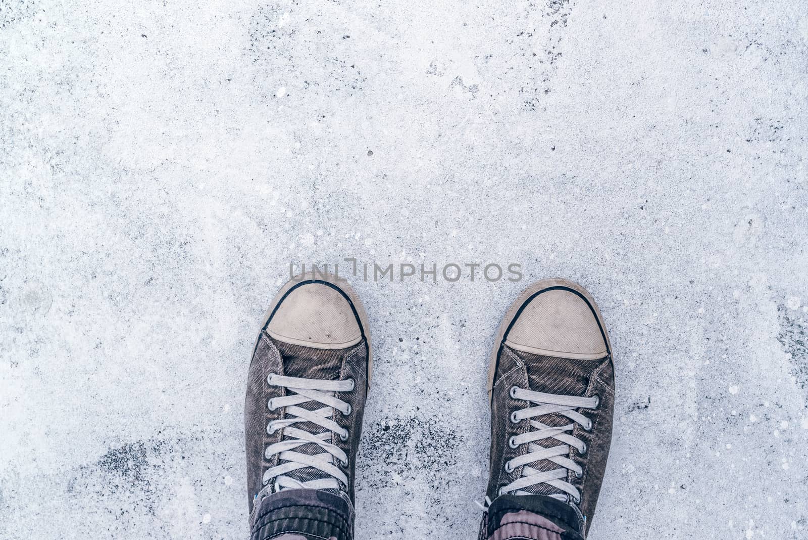 Top view of worn gray sneakers on white asphalt road by stevanovicigor