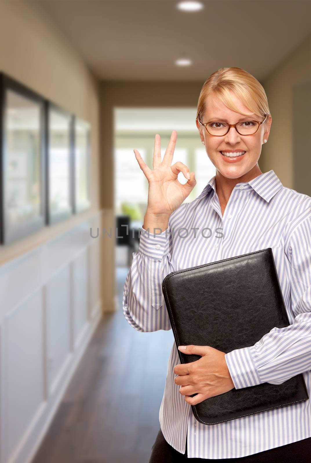 Smiling Businesswoman with Folder and Okay Hand Sign In Hallway of House.