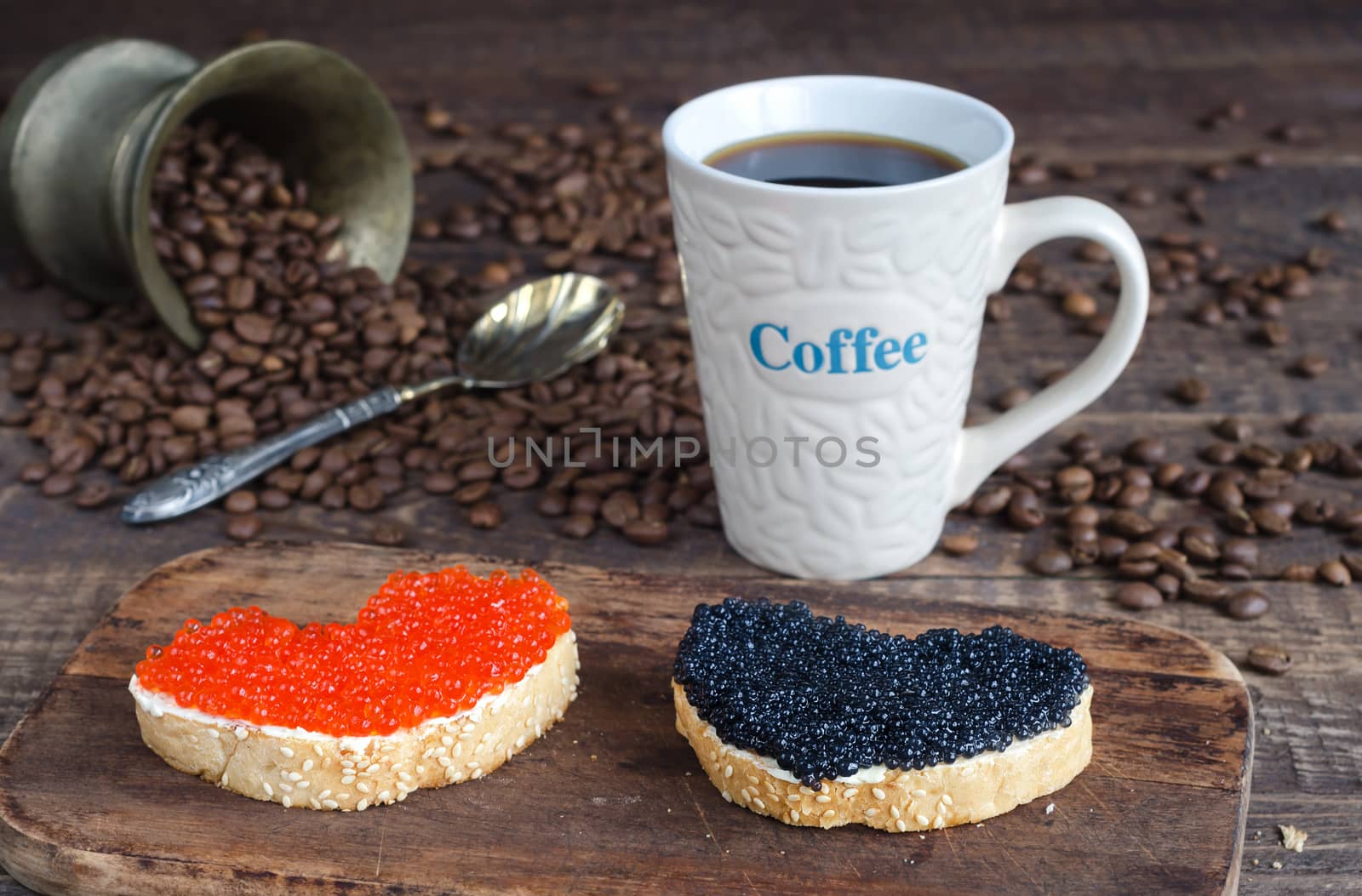 Sandwiches in the shape of a heart with black and red caviar and coffee in a mug with an inscription on the wooden surface. The roasted beans.
