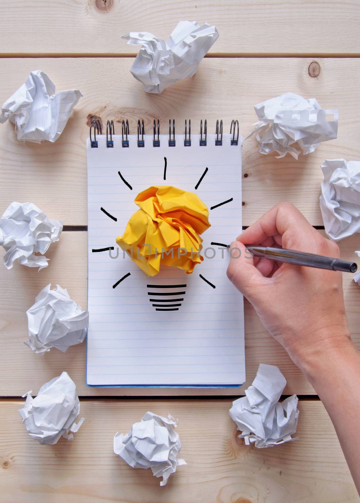 Drawing of a light bulb on a notepad with bright orange paper surrounded by crumpled pieces of paper 