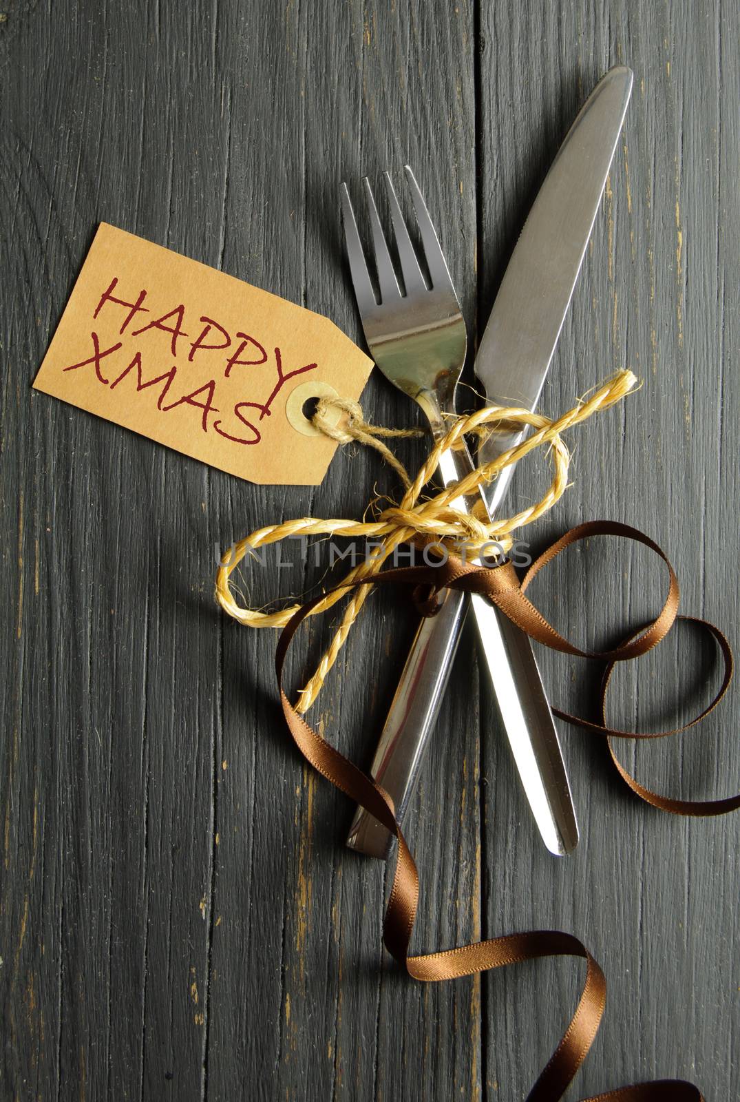 Fork and knife tied together on a wooden table background with christmas label