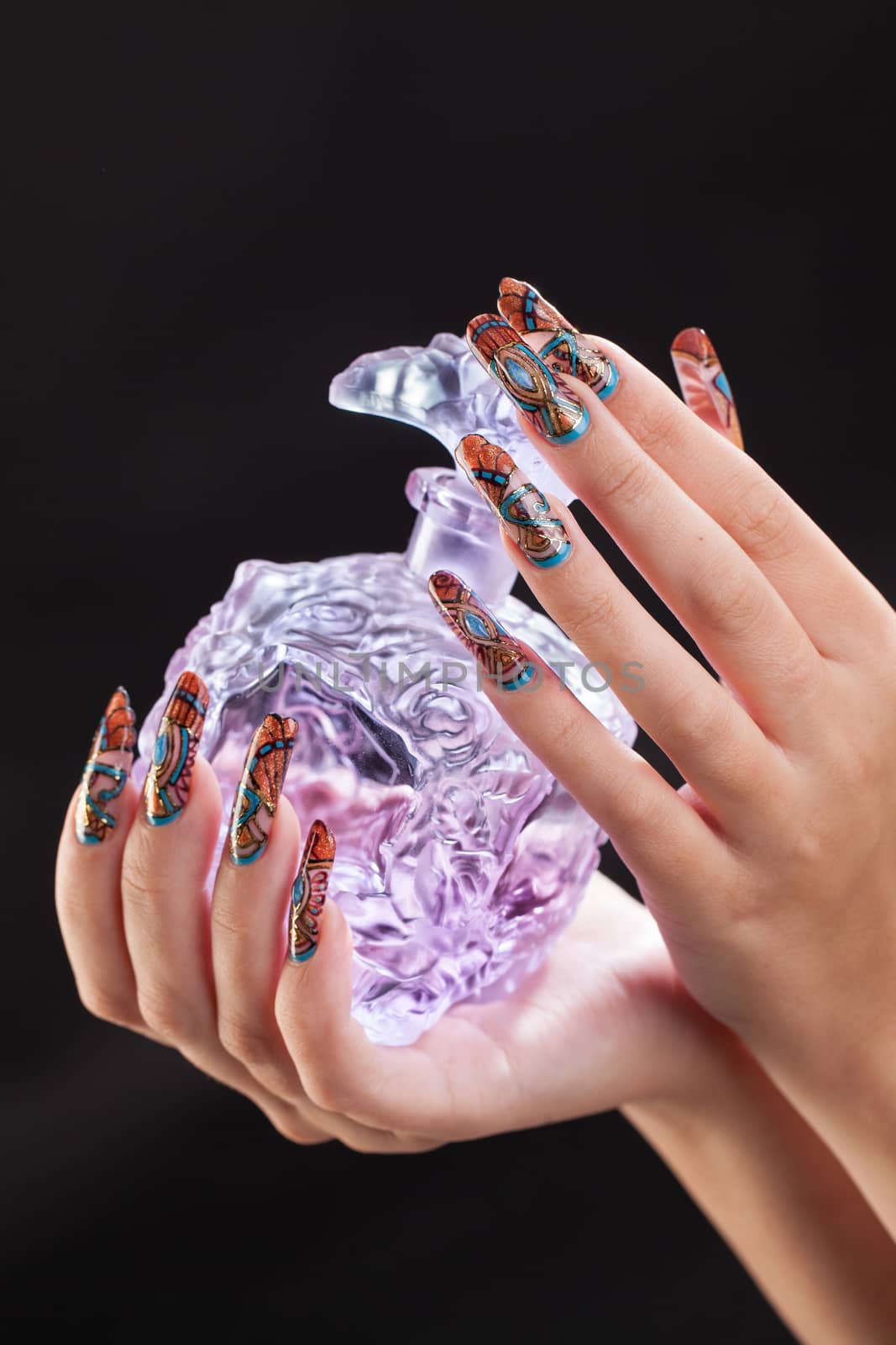 Woman's hands with artistic nail painting holding the glass on a black studio background