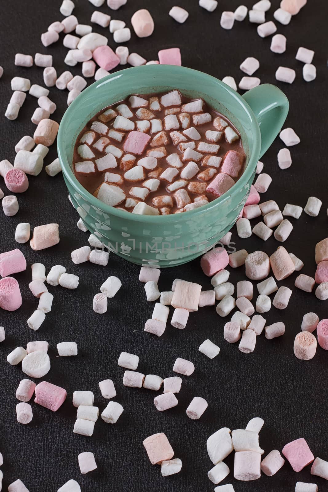Hot chocolate in a green cup with marshmallows scattered around. Black background
