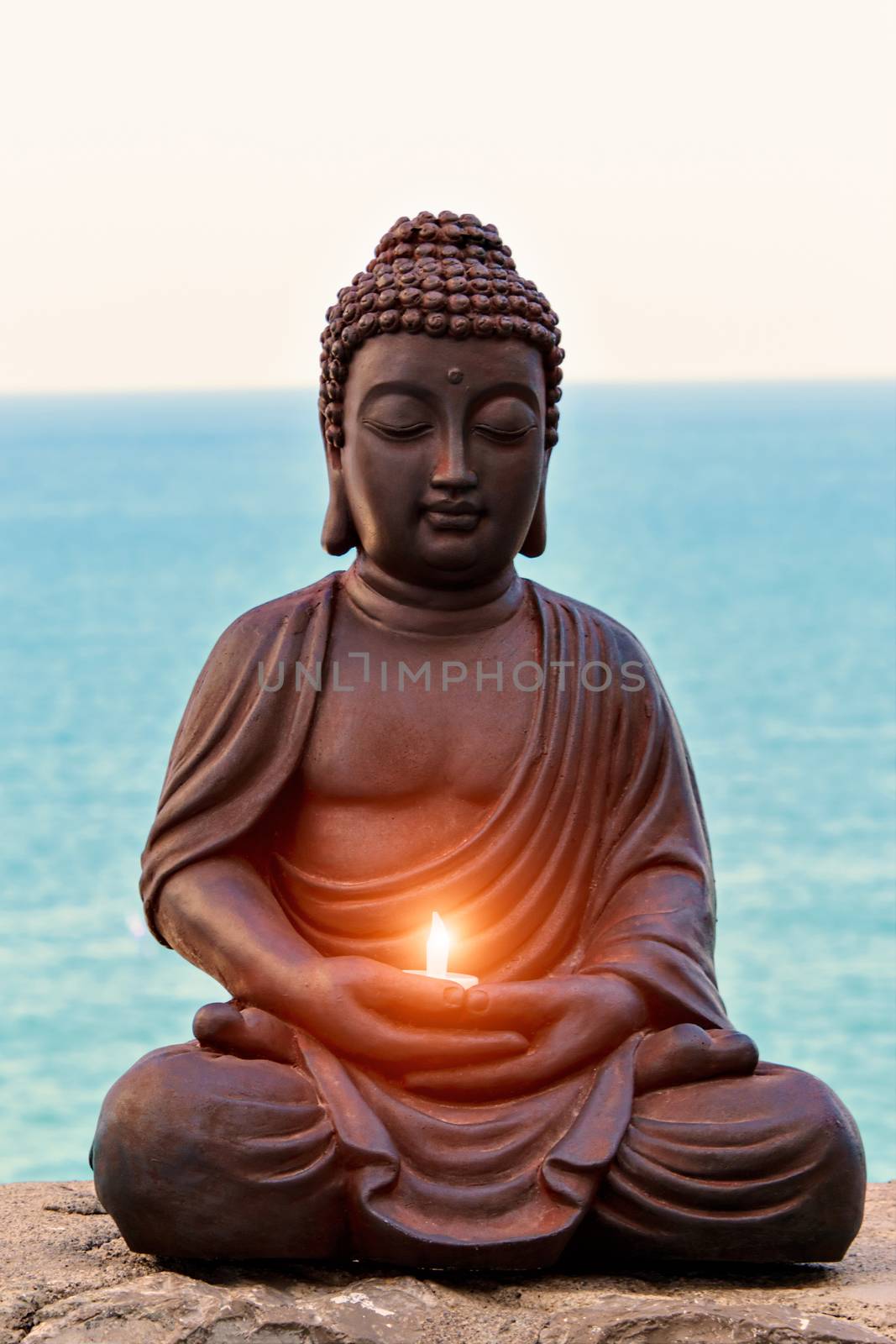 Buddha with a candle in hands and sea background. Vertical image.