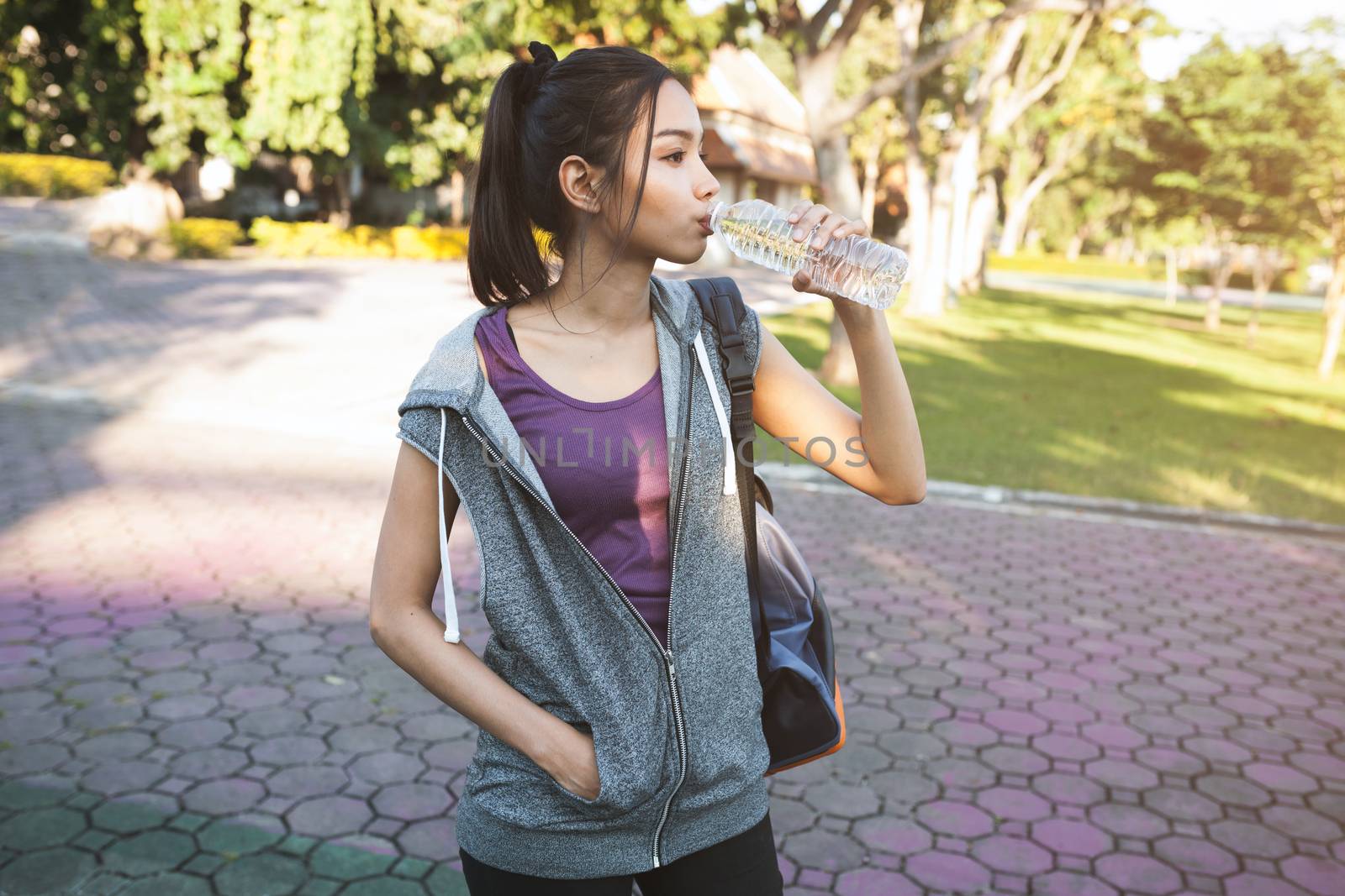 Portrait of young beautiful dark-haired woman in sport wearing drinking water at summer green park.