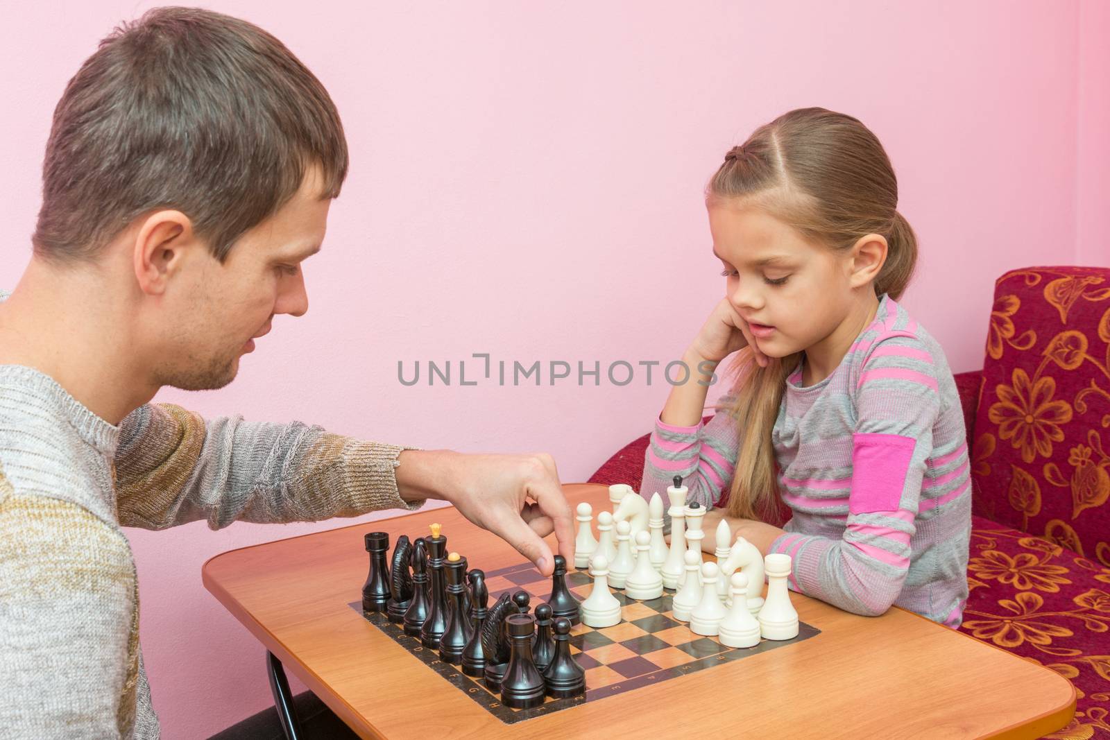 Dad teaches his daughter to make first moves in chess