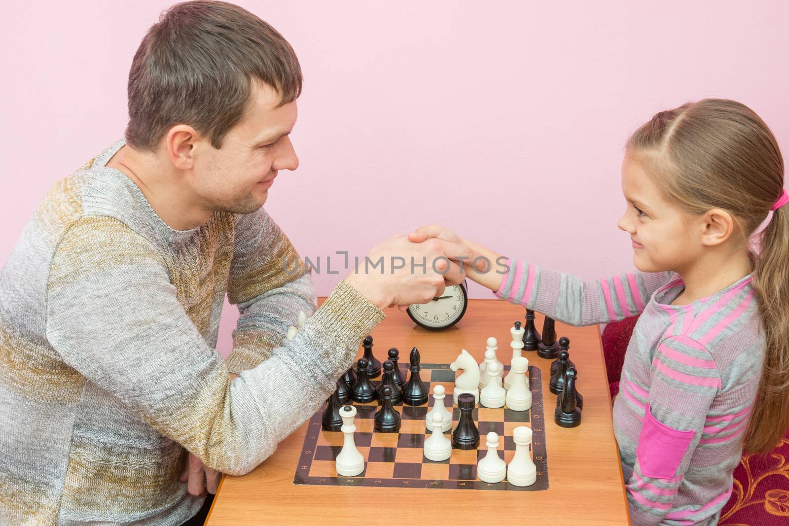 Dad and daughter shook hands, playing a game of chess