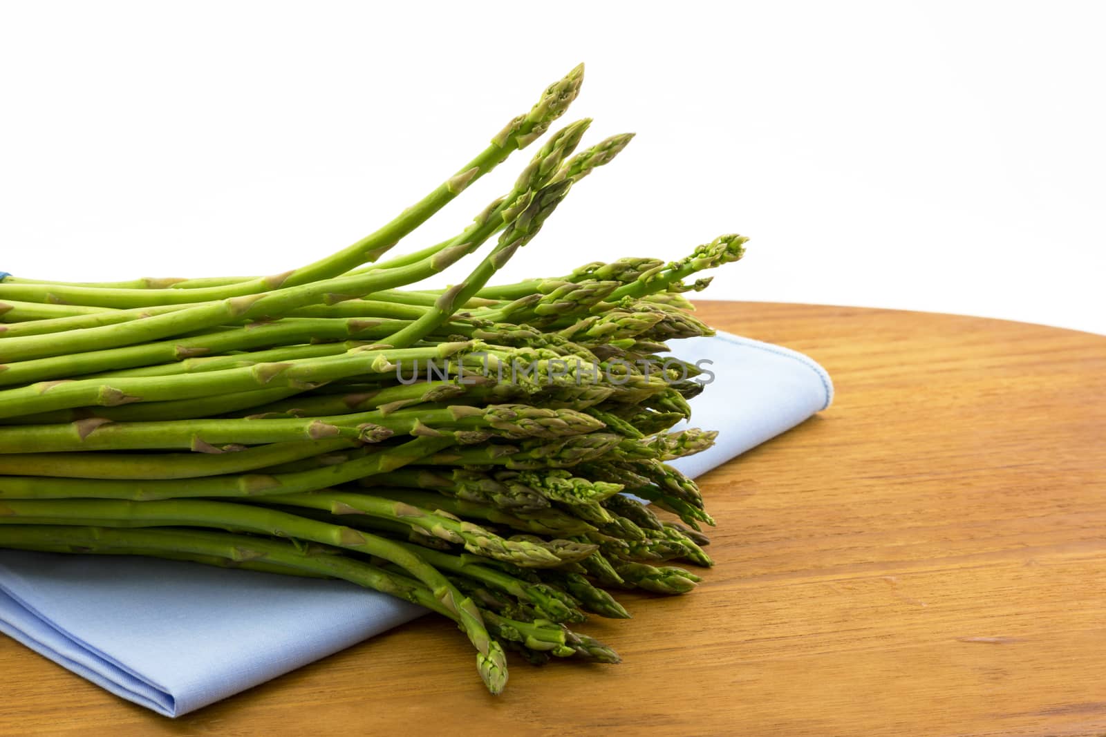 Fresh, uncooked asparagus placed on pale blue napkin  and wood board.  Horizontal image of garden vegetable with copy space. 