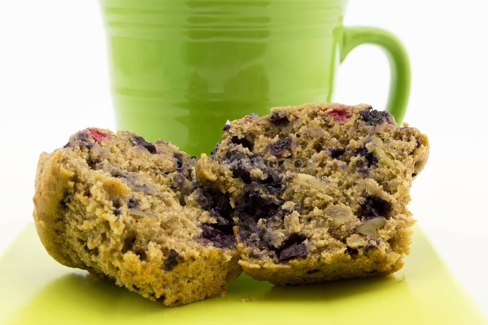 Delicious, healthy, whole grain muffin is  richly tasty with fruit and nuts.  Placed in front of hot coffee in green mug. Sliced muffin with crumbs on plate. 