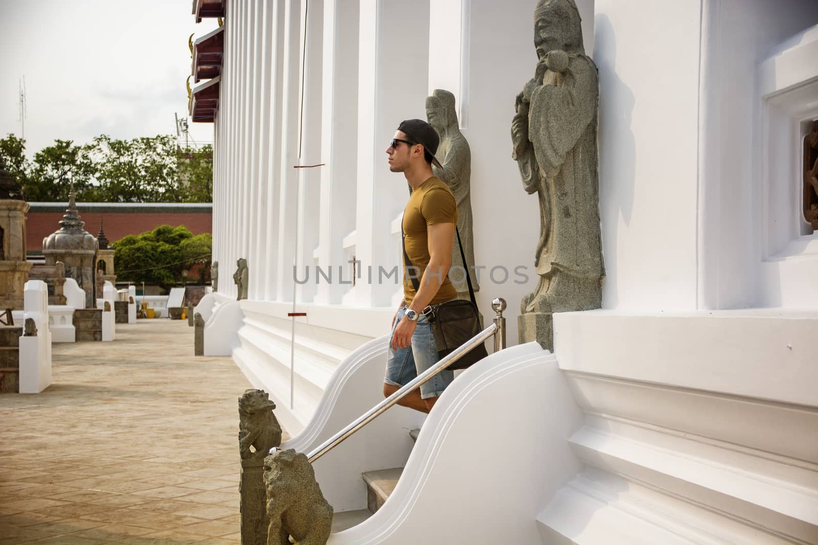 Side view of young man walking down stairs of buddhist temple in Bangkok, Thailand and looking straight.