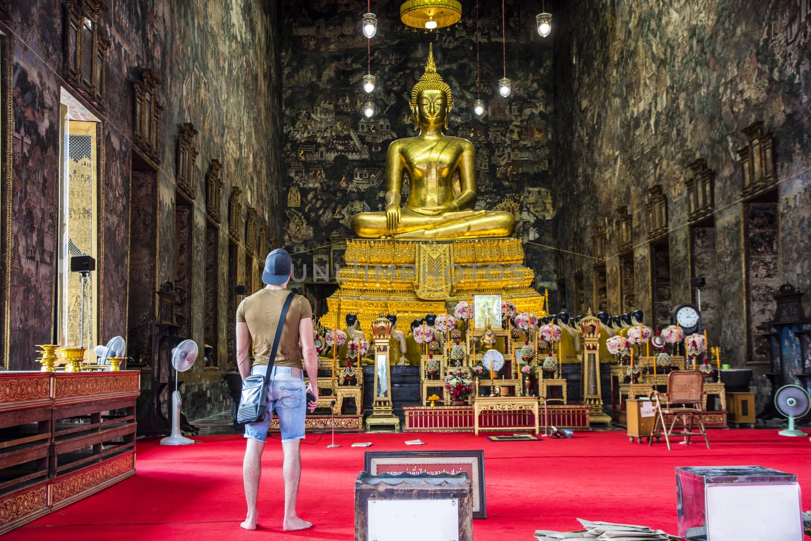 Back view of male standing inside of temple and looking at big statue of Buddha in Bangkok, Thailand