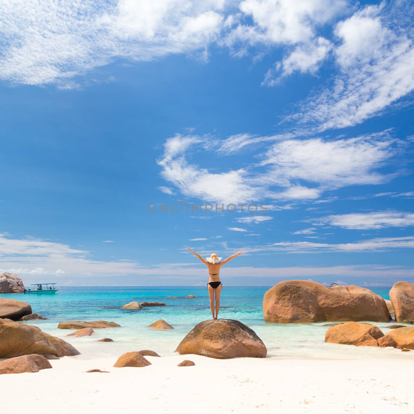 Woman, arms rised, wearing black bikini and beach hat, enjoying amazing view on Anse Lazio beach on Praslin Island, Seychelles. Summer vacations on picture perfect tropical beach concept. Copy space.