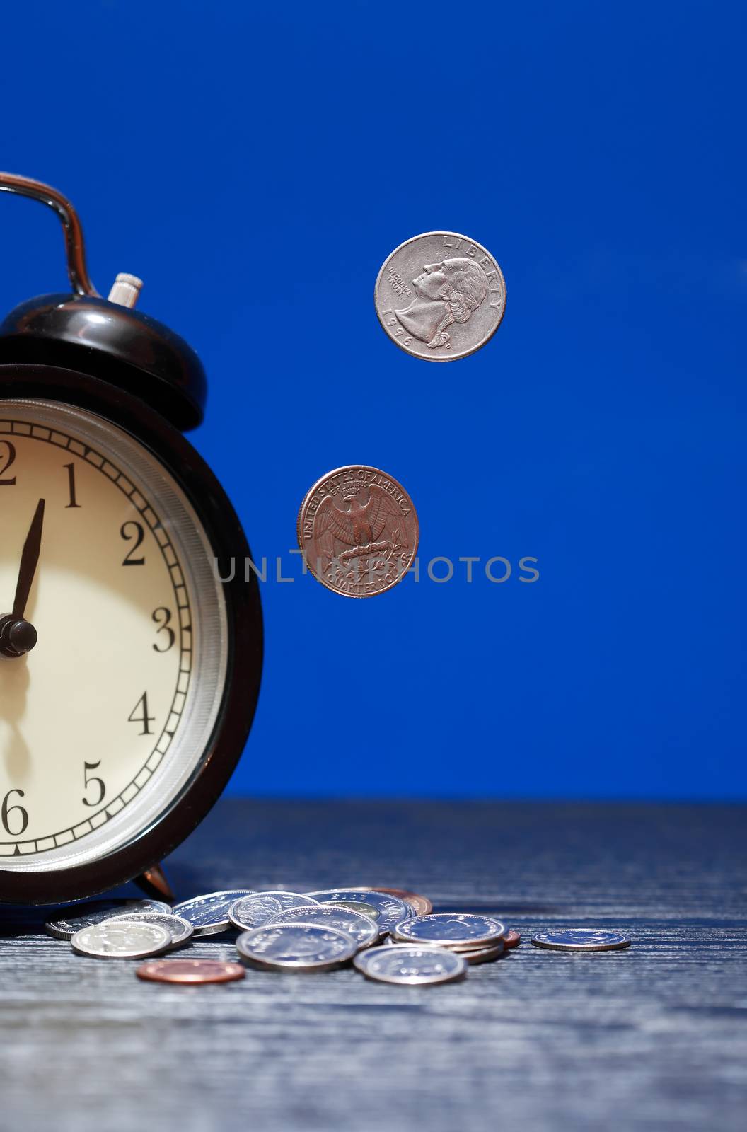 Time is money concept. Flying coins near alarm clock on dark background