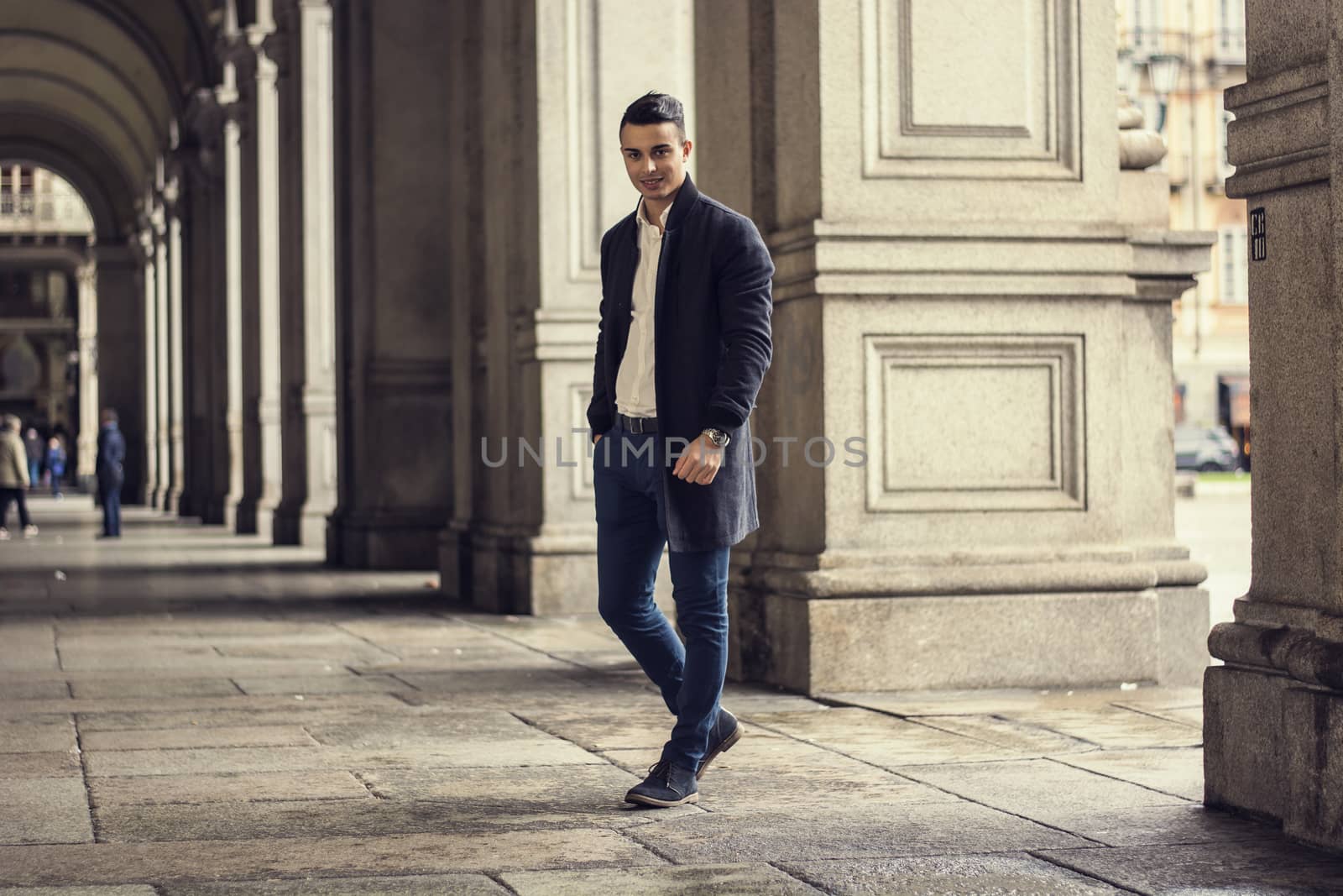 Trendy young man holding hand in pocket walking through gallery in Turin Italy and looking at camera.