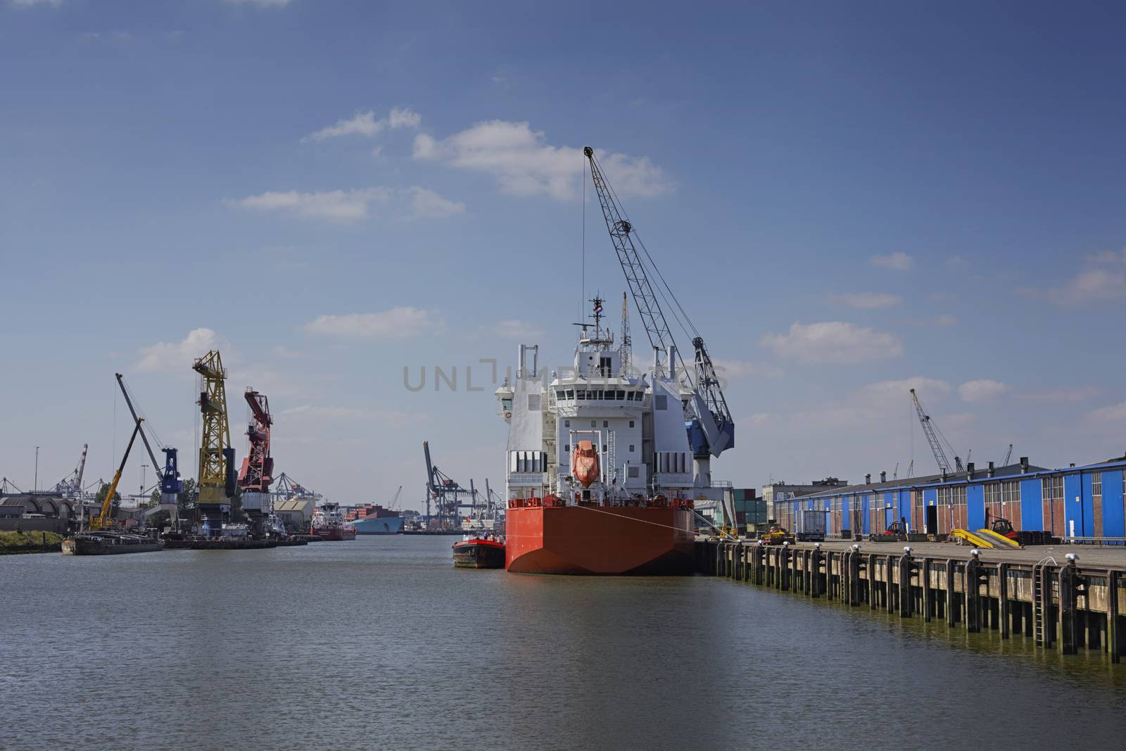 industrial ship with a life boat at a sunny day get unloaded in the port of rotterdam by janssenkruseproductions
