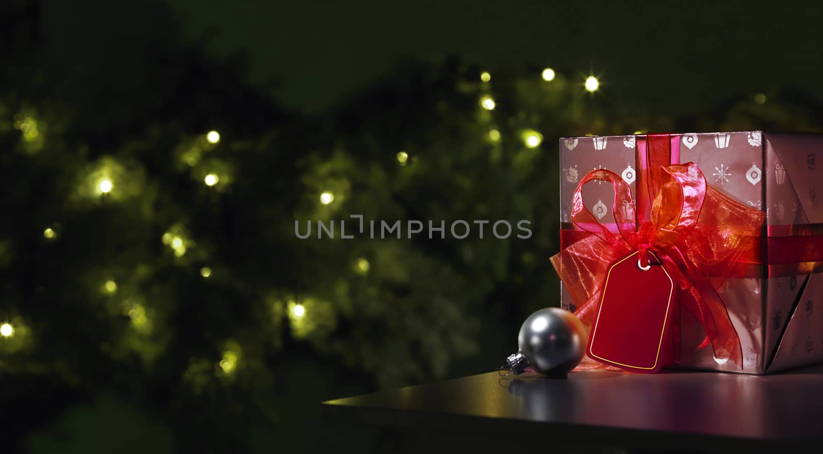 Red Christmas gift with a tree in the background wit a grey christmas ball