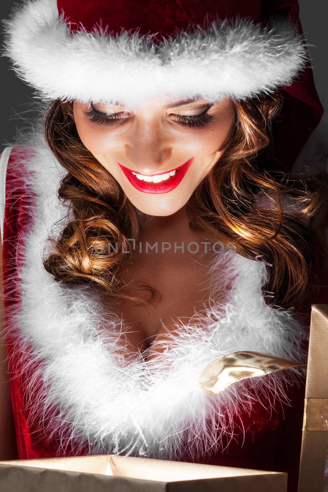 Beautiful woman in Santa Claus style costume looking into glowing Christmas gift box