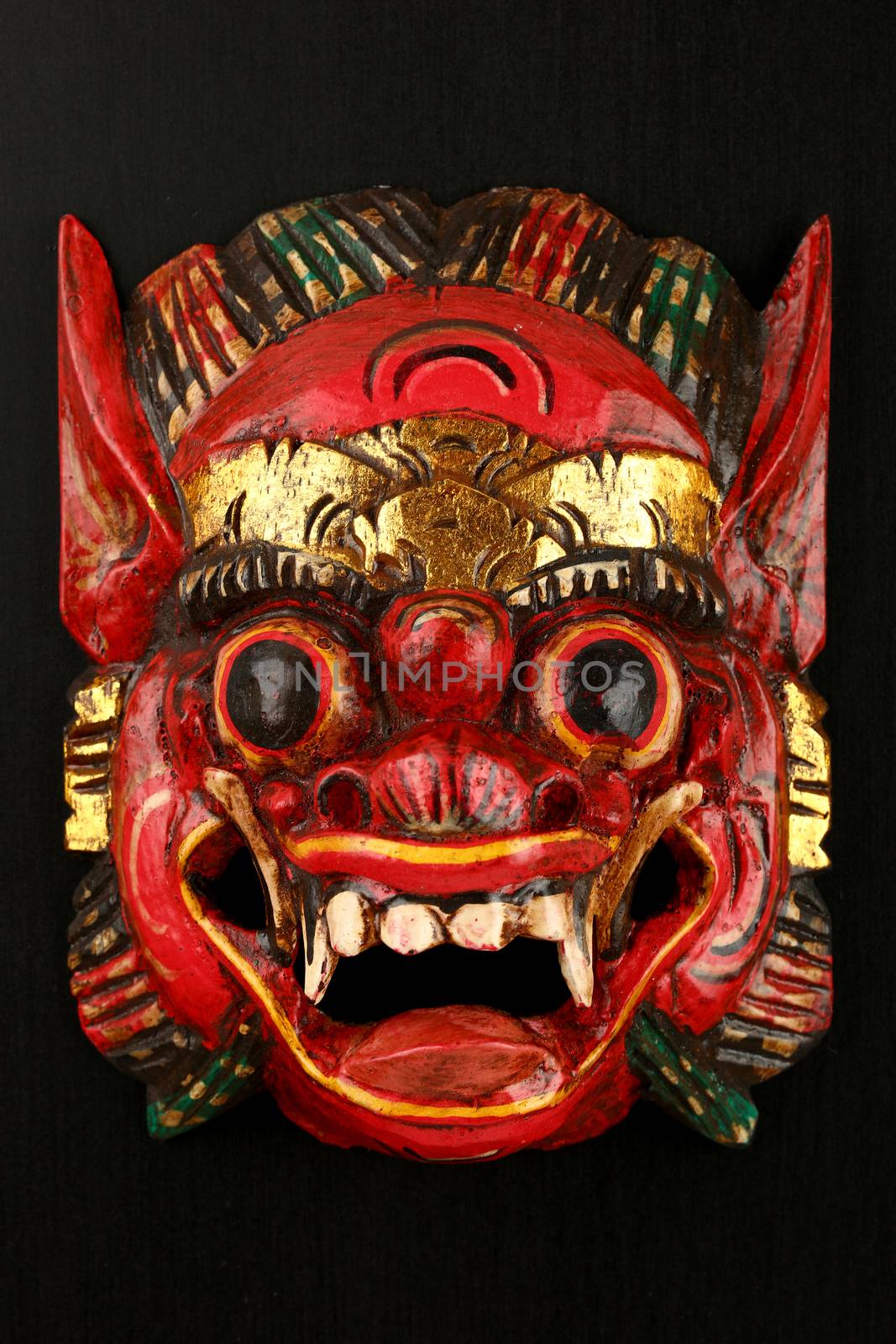 Asian traditional wooden red painted mask with face of demon, mythical lion or dragon painted on black background