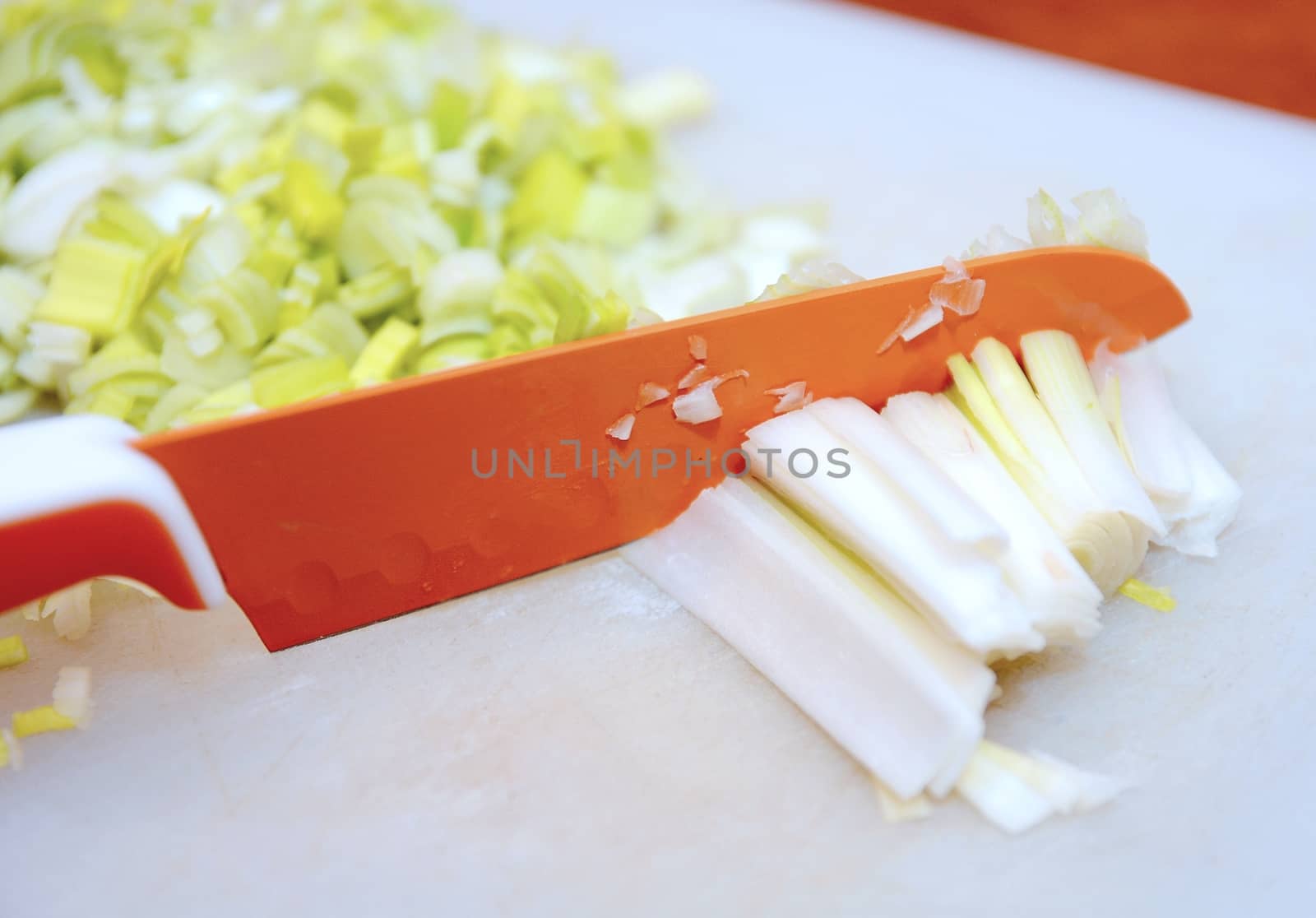 Closeup of knife cuts the fresh leek into small segments.