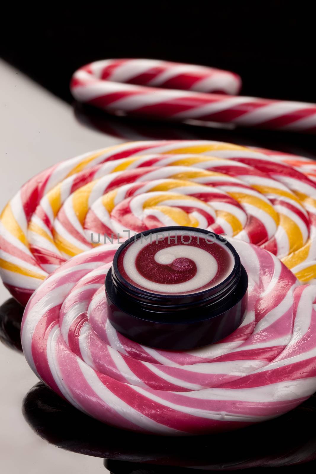 Cosmetic cream and lollipop on a glass studio background