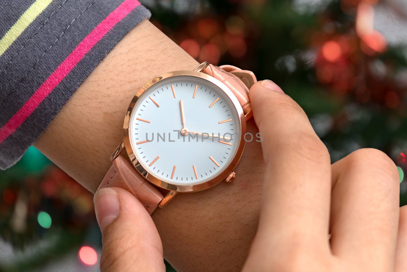 Girl's hand with wrist watch in Christmas time in front of Christmas tree in background