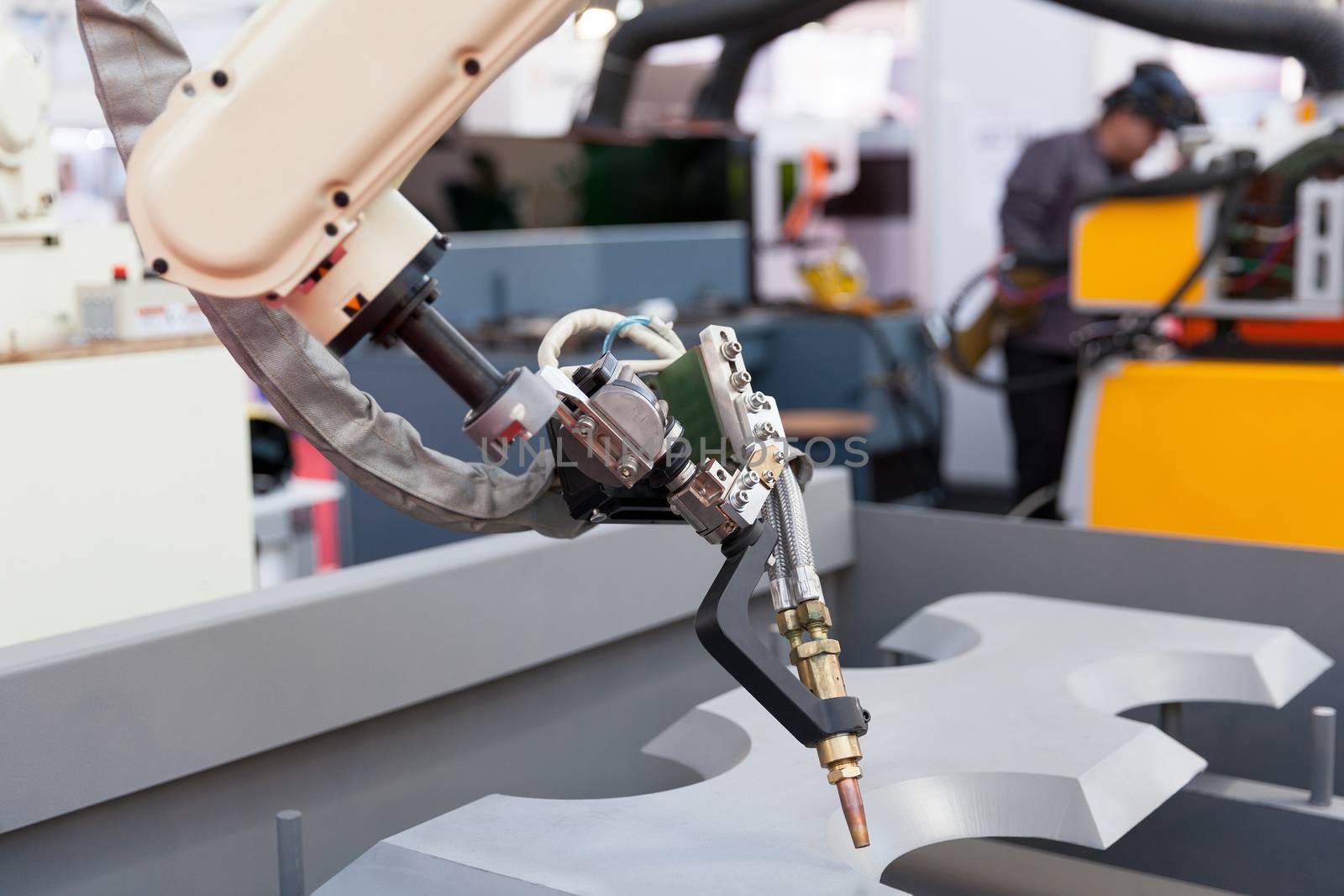 Industrial welding robot arm in the focus, blurred welder in the background by wellphoto